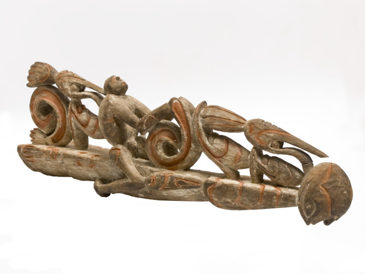 Voorsteven van een boomstamkano uit Sjuru, 1946-1956. Op de rug van de liggende mannelijke figuur zitten menselijke figuren en  jaarvogels. De menselijke figuren stellen dode voorouders voor. (TM-2540-82)